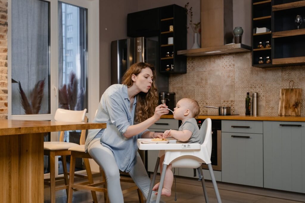 Mother feeding baby organic food in high chair in kitchen